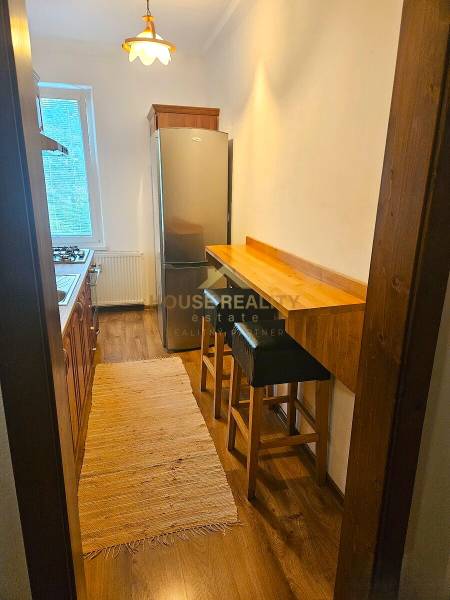 A narrow kitchen in a 3-room apartment with a gas stove, refrigerator, and a wooden decor floor.