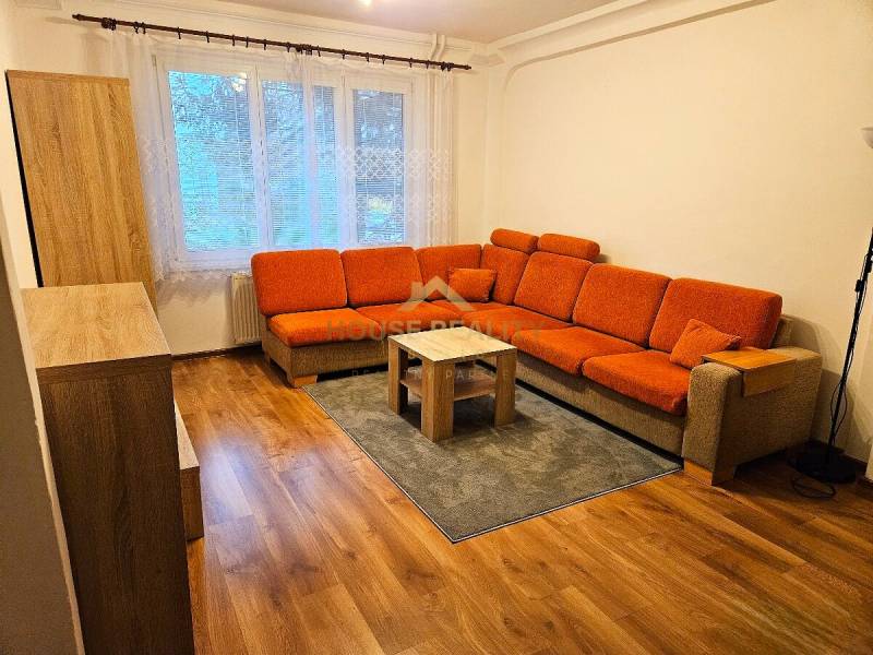 Living room with an orange sofa and wood-patterned flooring in a three-room apartment.
