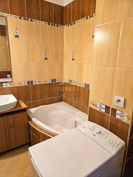 A bathroom with a corner bathtub, a washing machine, and a sink in a 3-room apartment.
