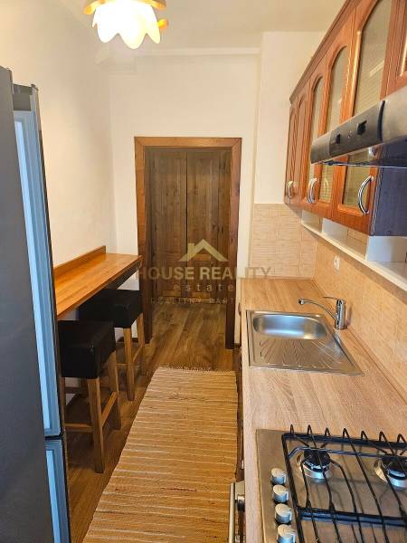 A kitchen in a 3-room apartment with a wood-patterned floor, a bar counter, and appliances.