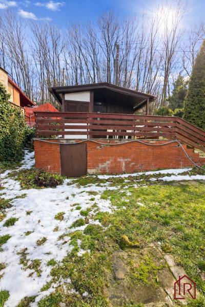 A cottage in Šemša surrounded by greenery and snow, with a terrace and a brick foundation.