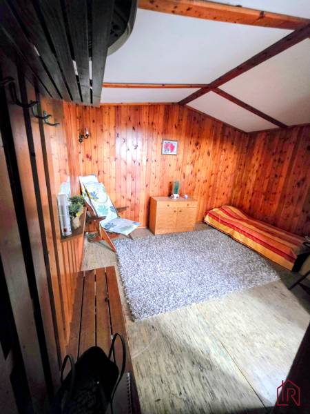 A room in a cabin with wooden paneling, an armchair, a bench, a carpet, and a bed.