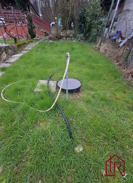 A garden by the cottage in Šemša, a lawn with a well and a hose.