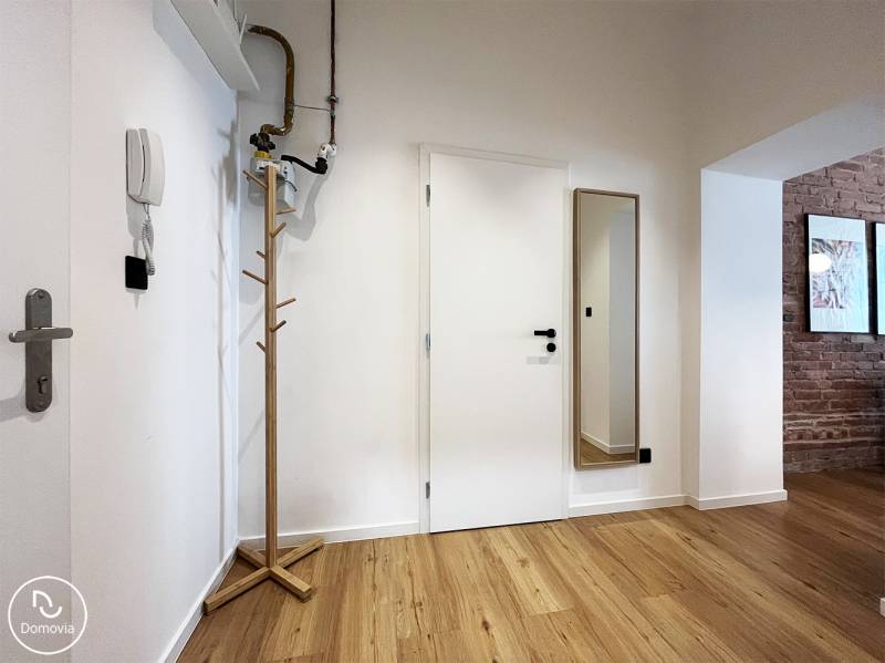 A hallway with a coat rack and a mirror, white walls, wooden floor, in a 2-room apartment on Vajnorská.