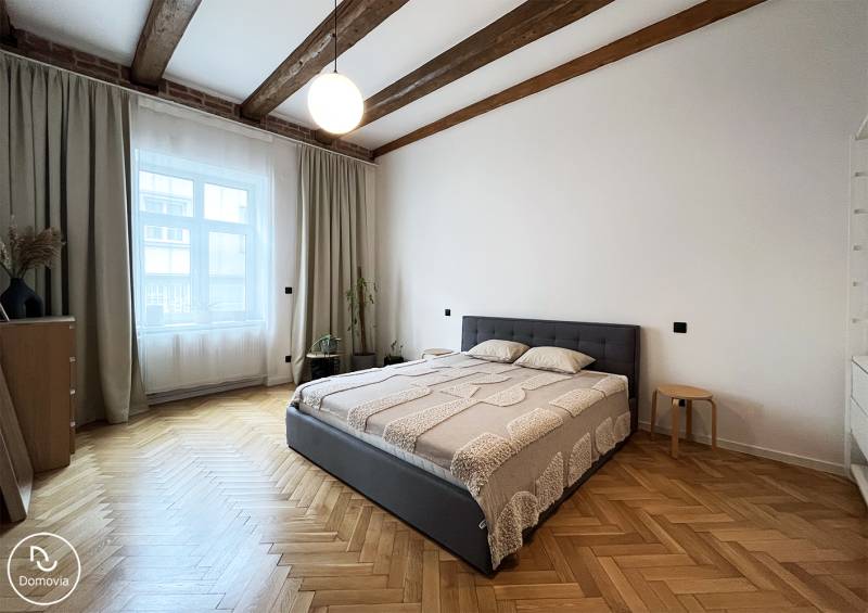 A bright bedroom with wooden beams, a comfortable bed, and parquet flooring on Vajnorská Street.