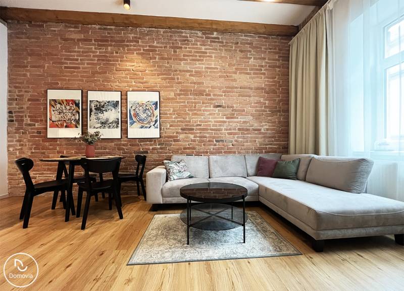 Living room with a brick wall, sofa, table, and paintings; bright space on Vajnorská Street, Bratislava.
