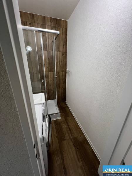 A bathroom in a studio apartment with a wooden decor floor, a shower corner, and a washing machine.