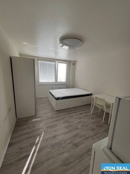 Studio apartment with a bed, wardrobe, table, and floor with a wooden decor.