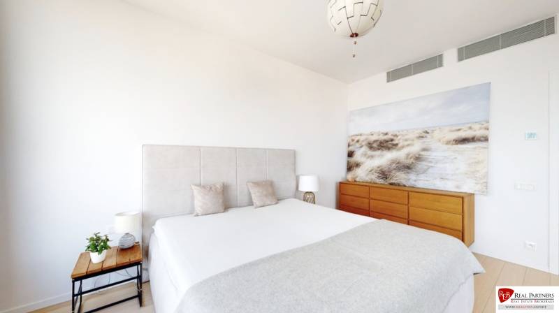 Bedroom in a 3-room apartment with a large bed, a painting, and a wooden dresser.