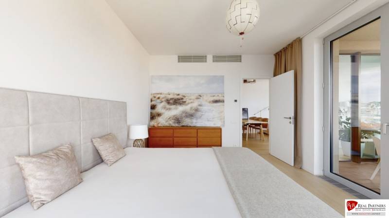 A bedroom with an upholstered headboard, a painting above the dresser, and glass doors in a three-room apartment.
