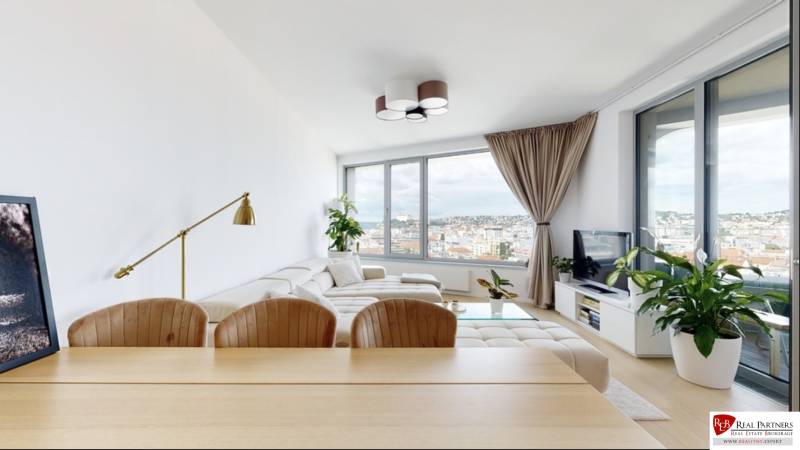 Living room of a three-room apartment with a light-colored sofa, large windows, and a view of the city.