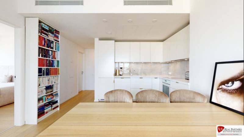 A kitchen in a 3-room apartment with built-in appliances, a dining table, and a bookshelf.