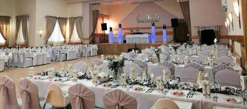 A banquet hall prepared for a wedding reception, tables adorned with white tablecloths.