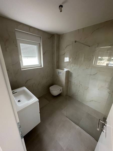 Bathroom in a 3-room apartment with a sink, toilet, and shower enclosure with a glass wall.