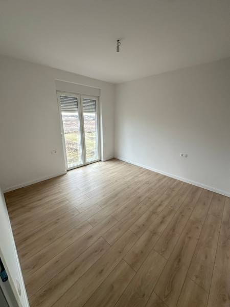 An empty room in a 3-room apartment with a wood-patterned floor and a French window.