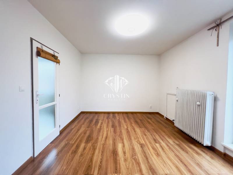 A room in a 2-room apartment with a wooden decor floor and a radiator.
