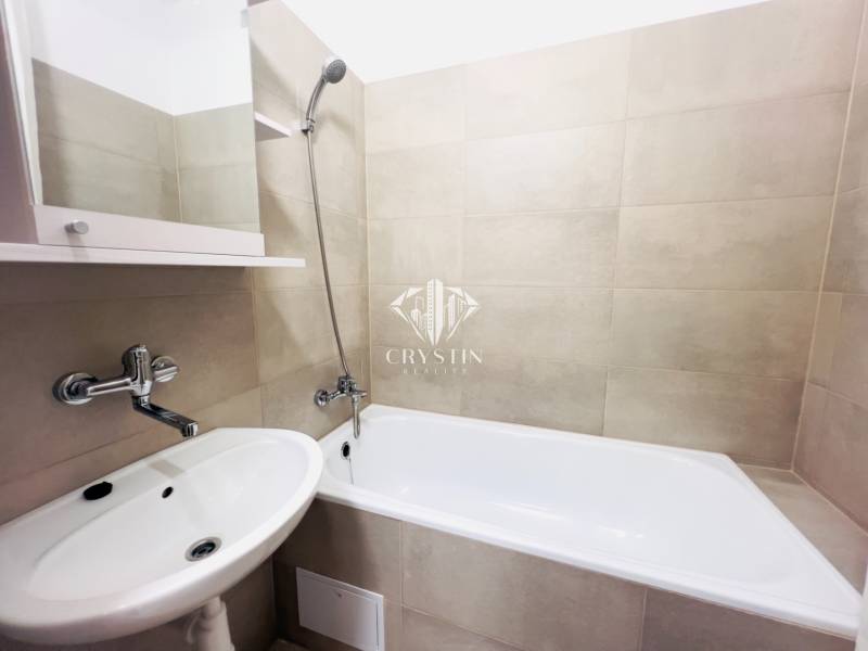 Bathroom in a 2-room apartment with a bathtub, sink, and light ceramic tiles.