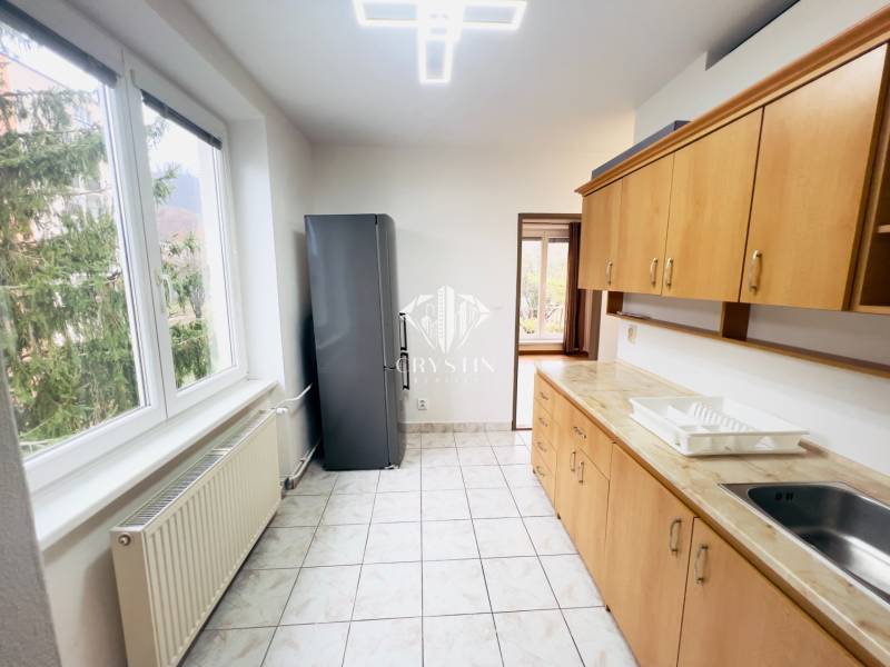 A kitchen in a 2-room apartment with windows, tiles, and wooden decor cabinets.