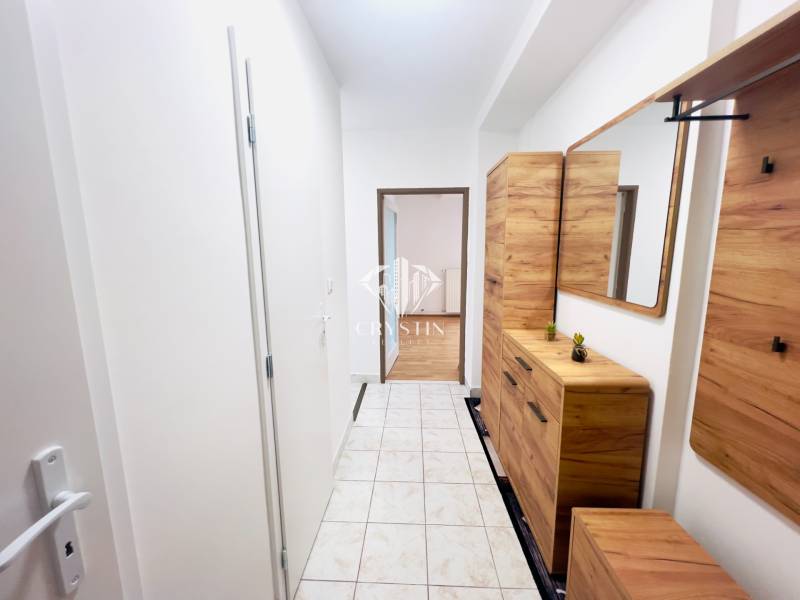 A hallway in a 2-room apartment with tiled flooring and wooden decor furniture.