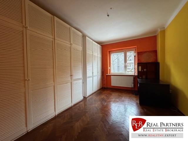 A room with an orange wall, a large wardrobe, and a wooden-patterned floor in a 3-room apartment.
