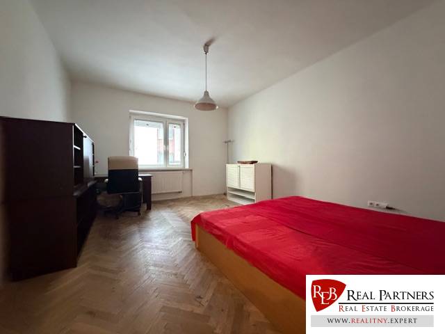 Bedroom in a 3-room apartment with a bed, desk, and wooden decor flooring.