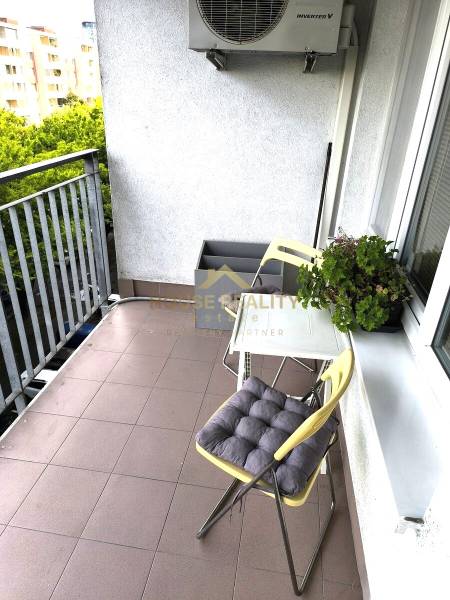 A balcony of a 2-room apartment with seating and greenery, ideal for relaxation.