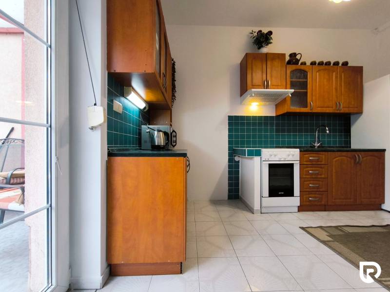 A kitchen in a family house with wooden cabinets, green tiles, and a white stove.