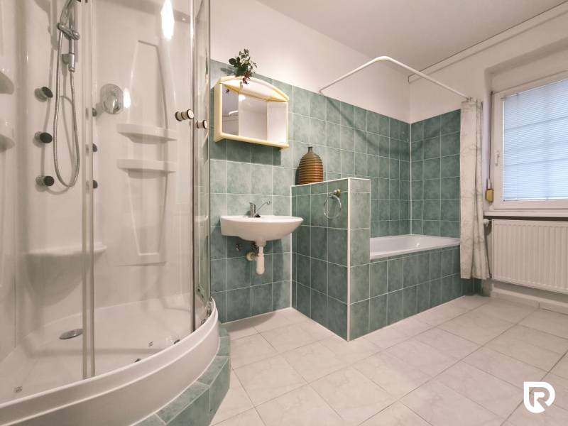 Bathroom in a family house with a bathtub, shower, sink, and tiled walls.