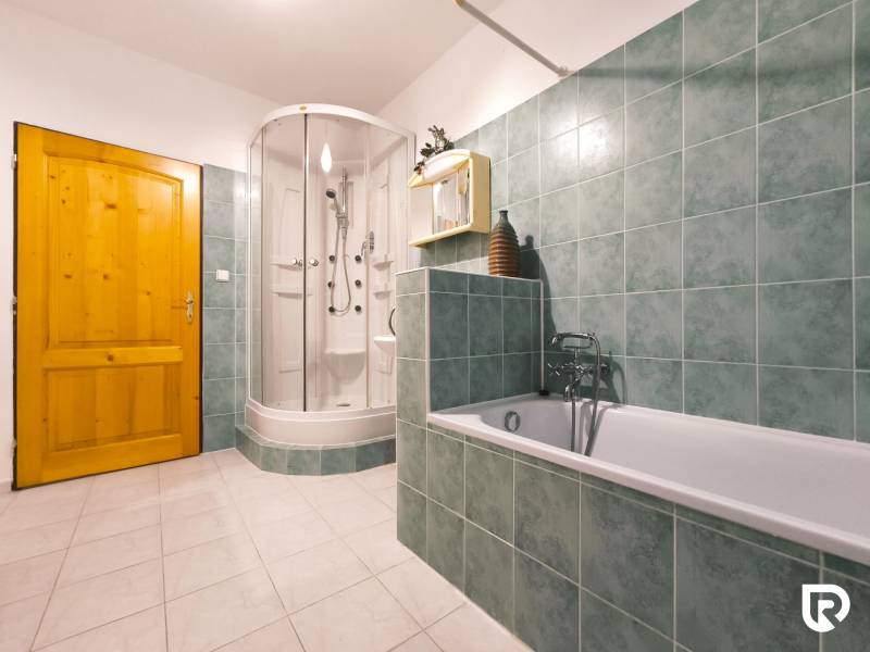 A bathroom in a family house with a bathtub, a shower corner, and green tiles.
