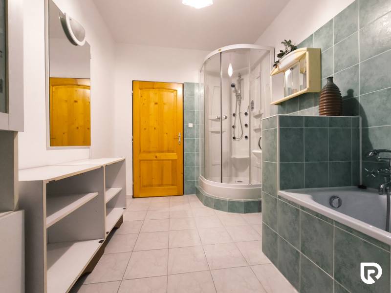 Bathroom with a bathtub and a shower in a family house. Green tiles and white cabinets.