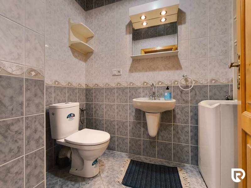 Bathroom in a family house with tiles, toilet, sink, and mirror.