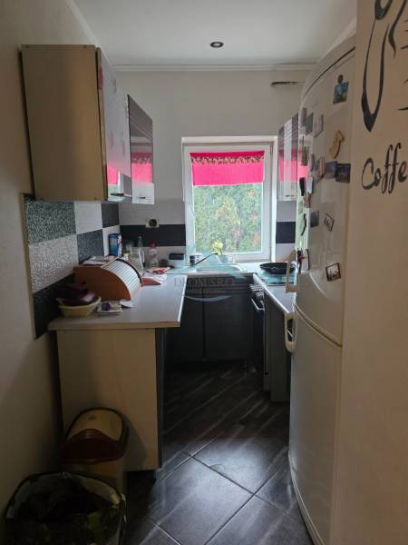 A narrow kitchen with black and white cabinets and a large white refrigerator in a family house.