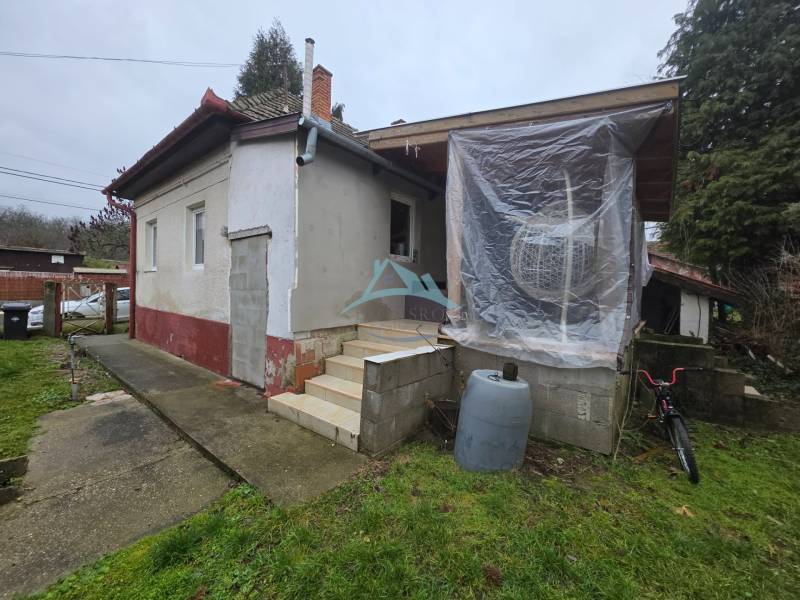 A family house in Hont with an unfinished facade, plastic windows, and stairs at the entrance.