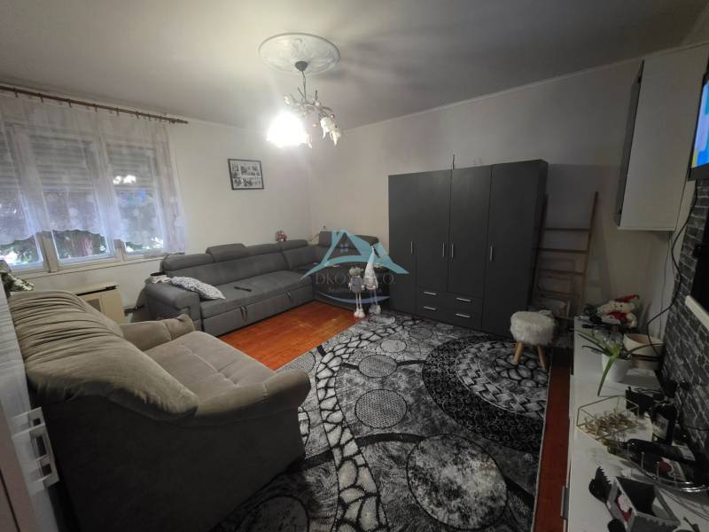 Living room in a family house with a gray sofa and a wooden-patterned floor.