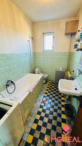 A bathroom in a family house with a bathtub and a window, with colorful tiles and green wall tiles.