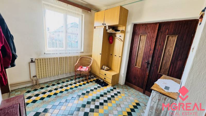 Entrance hall in a family house with a colorful tiled floor, a cabinet, and a wicker chair.
