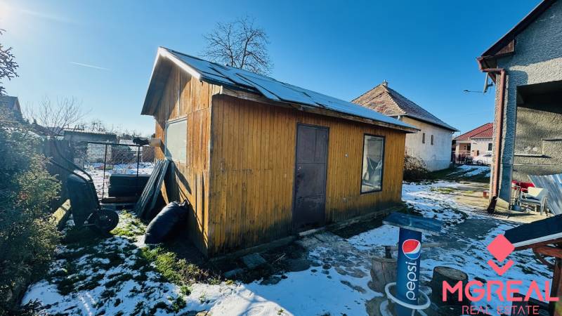 Behind the house in Partizánske, Veľké Bielice, there is a wooden cabin in the snowy yard.