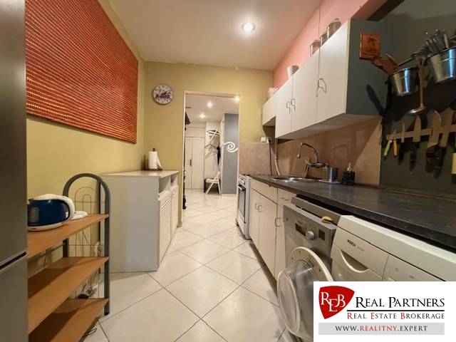 A kitchen in a 5 or more room apartment with white cabinets and tiles, appliances on both sides.