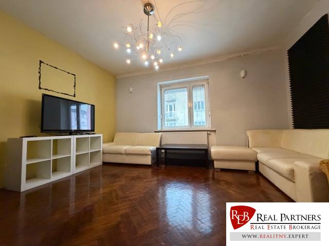 Living room with white sofas, wood-patterned flooring, and a light chandelier in a three-room apartment.