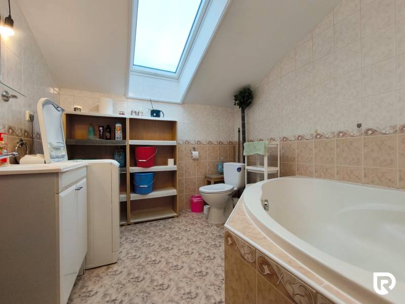 A bathroom in a family house with a bathtub, washing machine, shelf, and skylight.