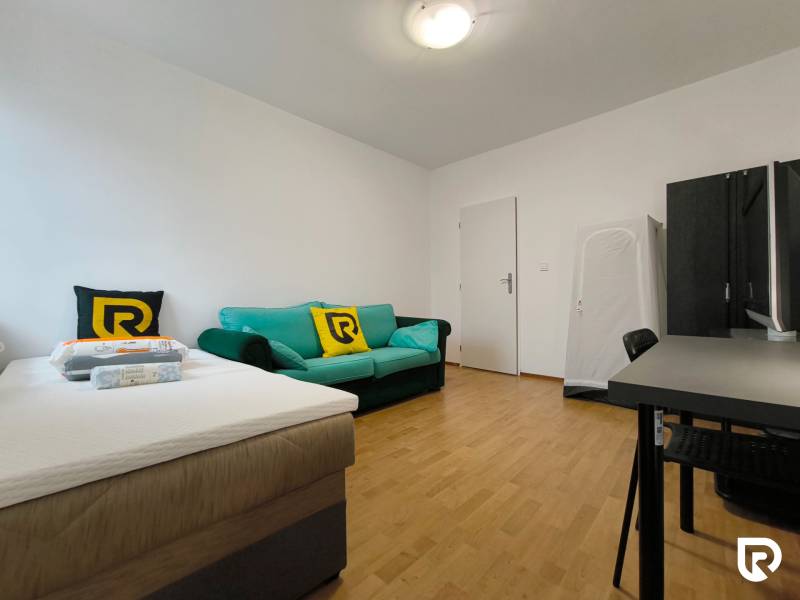 A room in a family house with a bed, a sofa, and a desk, with a wooden-decor floor.