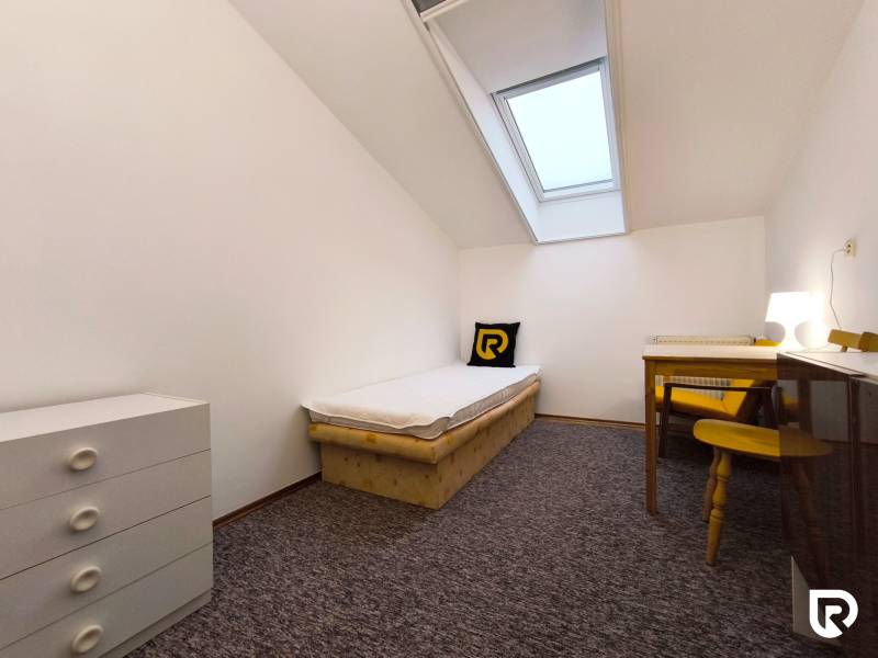 A simple room with a single bed, a table, and a dresser in a family house.