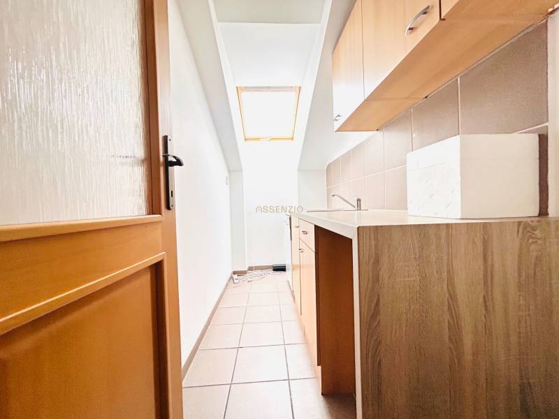 A narrow kitchen area in the office with a window and a wooden decor floor.