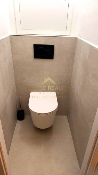 A bathroom with a wall-mounted toilet and gray tiles in a 3-room apartment.