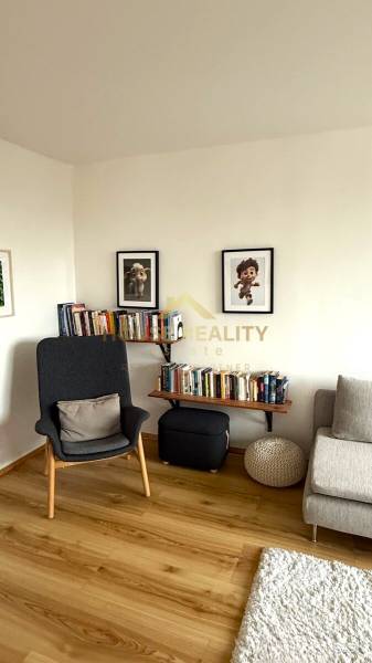 Living room with an armchair, a bookshelf full of books, pictures, and a floor with a wooden decor.