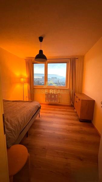 Bedroom with a table in a 3-room apartment, with a wood-patterned floor and a view from the window.
