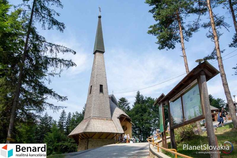 The church in the recreational grounds of Litmanová surrounded by trees and an information board.
