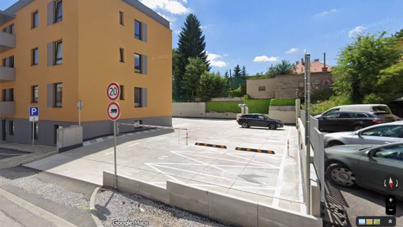Parking lot and residential building on Rudlovská Road in Banská Bystrica surrounded by greenery.