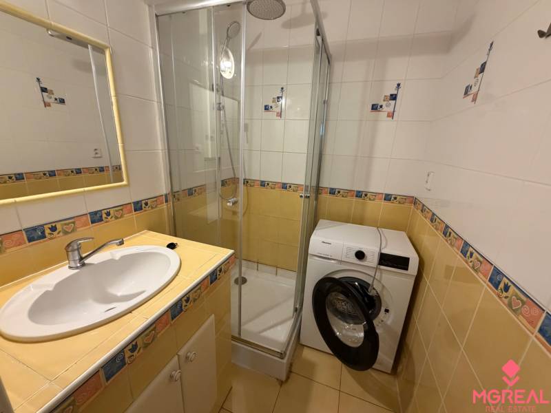 Bathroom in a 3-room apartment with a sink, shower, and washing machine, yellow and white tiles.