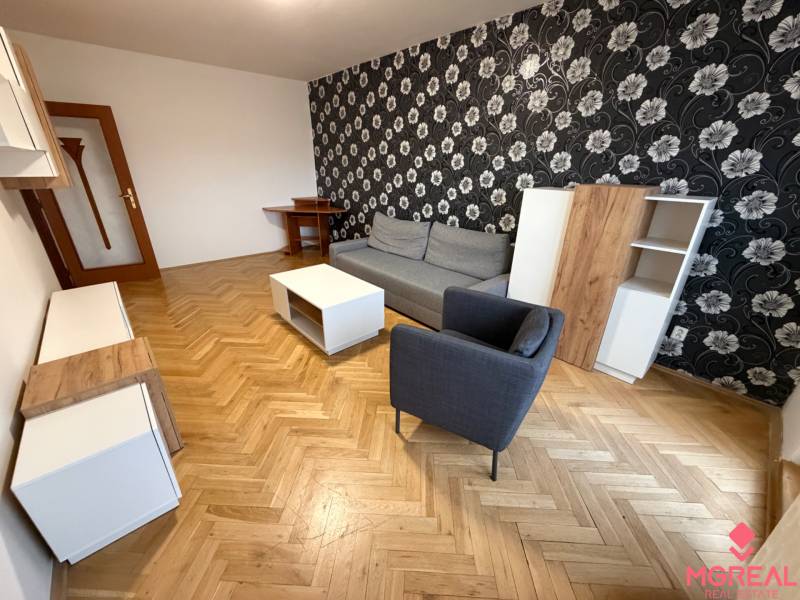 Living room in a three-room apartment with a wooden-patterned floor, patterned wallpaper, and furniture.